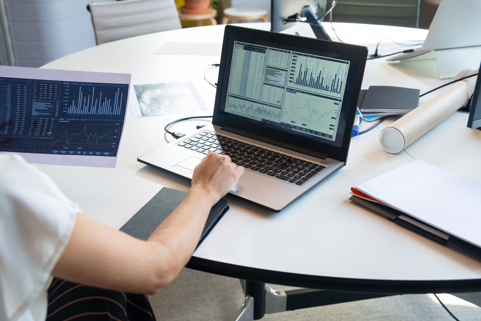A person reviewing financial charts on a laptop and printed paper at a desk